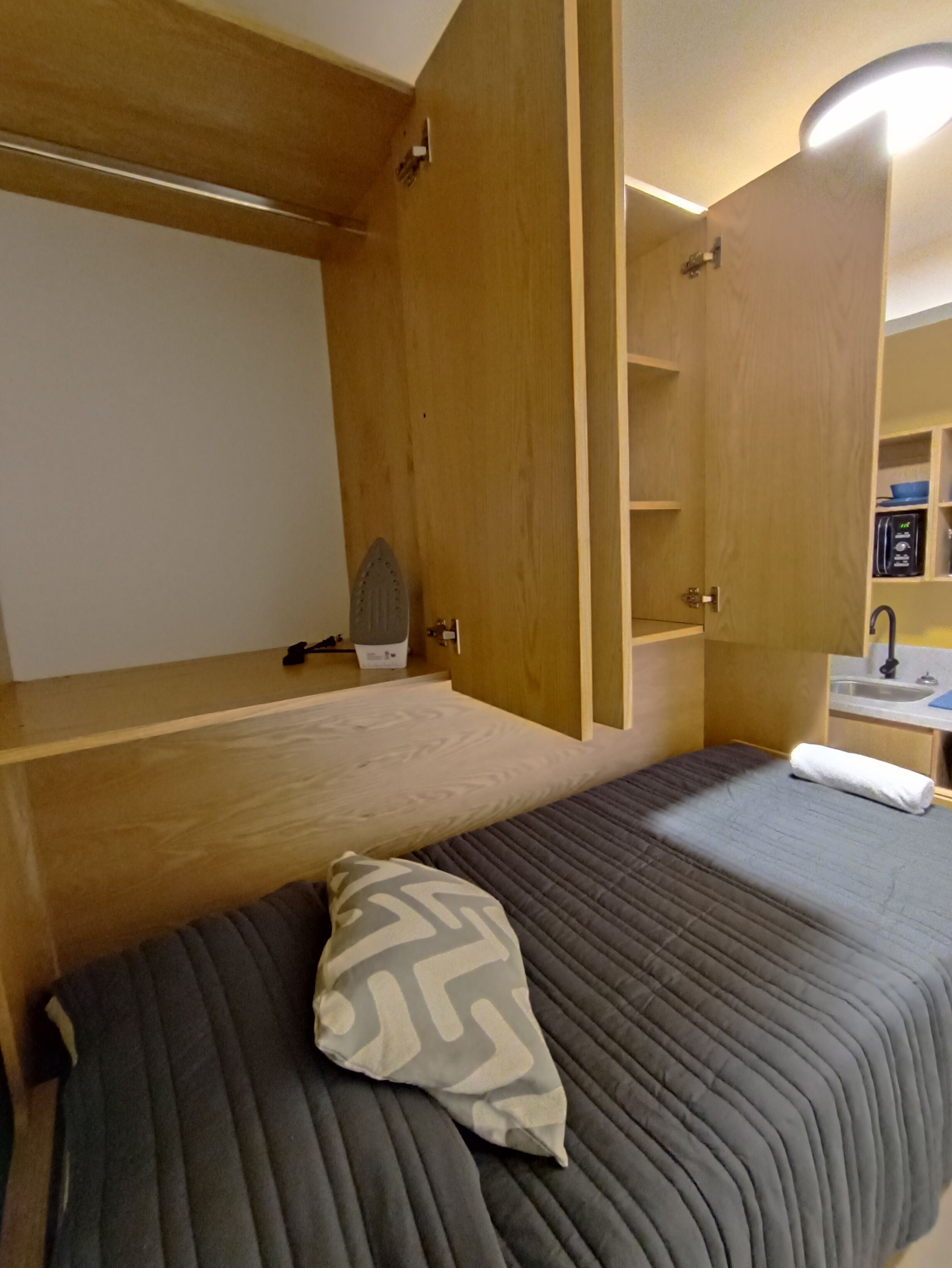 Una habitación compacta con una cama, un escritorio pequeño y una estantería empotrada.