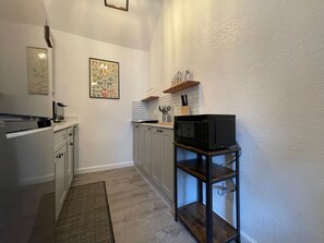 Cocina compacta con un microondas en un estante de madera, un lavamanos pequeño y una planta decorativa.