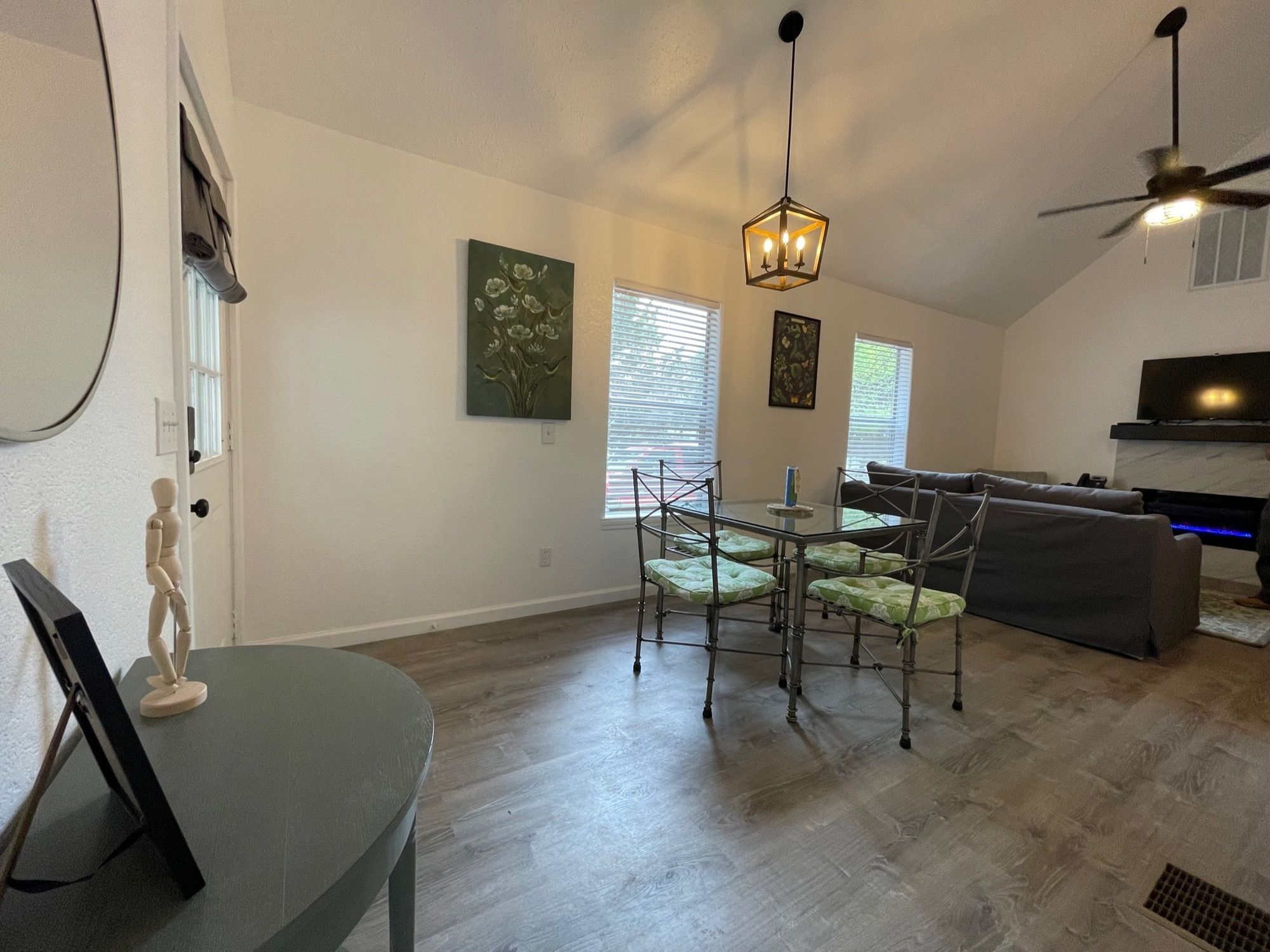 A dining area with a table and chairs, a sofa, a television, and artwork on the walls.