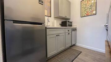 A compact kitchen with a stainless steel refrigerator, a microwave, and a sink. There is a small countertop with a toaster and a cabinet above it. A welcome sign is visible on the wall.