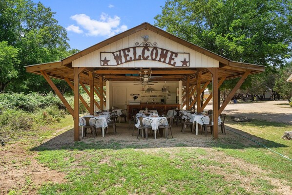 Un pabellón de madera con un letrero que dice 'WELCOME', mesas con manteles y una zona de cocina.