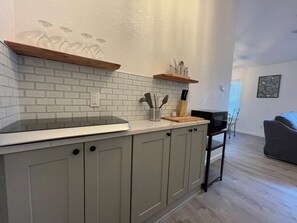 Une cuisine avec un mur recouvert de briques blanches, des armoires grises et un plan de travail en bois. On peut y voir un four à micro-ondes, un bloc à couteaux et une chaise.