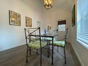 Un comedor con una mesa y sillas de madera, láminas botánicas enmarcadas en la pared, y una ventana con persianas.