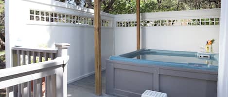 A hot tub under a wooden pergola with a white fence and a small white stool.