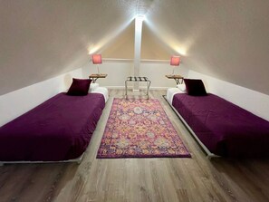 Une chambre avec deux lits, un tapis au centre et un luminaire au plafond.