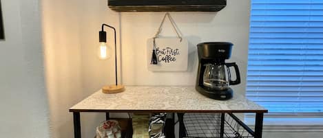 A kitchen counter with a coffee maker, a hanging sign, and a light fixture.