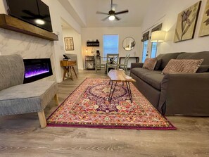 A living room with a fireplace, a sofa, a coffee table, and a patterned rug. - Cottage 6 Purple, Pet-Friendly One-Bedroom Cottage with Loft, Hot Tub (Wimberley)