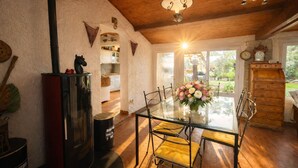 A rustic kitchen with a wooden ceiling, a glass dining table with yellow cushioned chairs, a decorative flower vase, and a wooden cabinet with a clock. - "La Désirée" air-conditioned bastidon, private estate, swimming pool, pétanque, restaurant. (Fréjus)