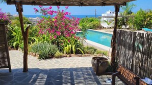 Un espace piscine avec vue sur l’océan, entouré de plantes tropicales et agrémenté d’une pergola en bois.