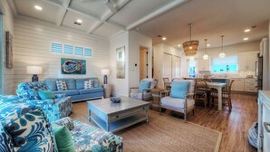 A spacious living room with a sofa, armchairs, and a coffee table. There is a kitchen area with a dining table and chairs. - Southern Cross by Avantstay Steps to the Beach, Pool, Fire Pit & Direct Boardwalk Access (Port Aransas)
