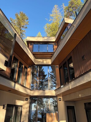 Un bâtiment moderne doté d’un atrium central, de grandes fenêtres et offrant une vue sur les arbres et le ciel.