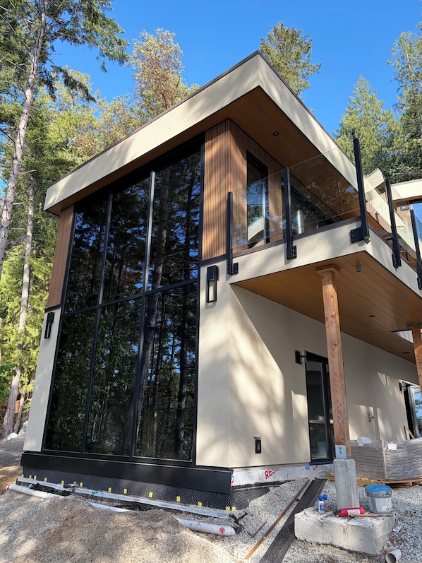 A modern two-story house with large windows, a flat roof, and a wooden deck.