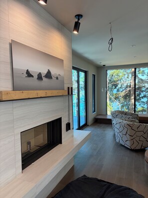 A modern living room with a fireplace, large windows, and a patterned sofa.
