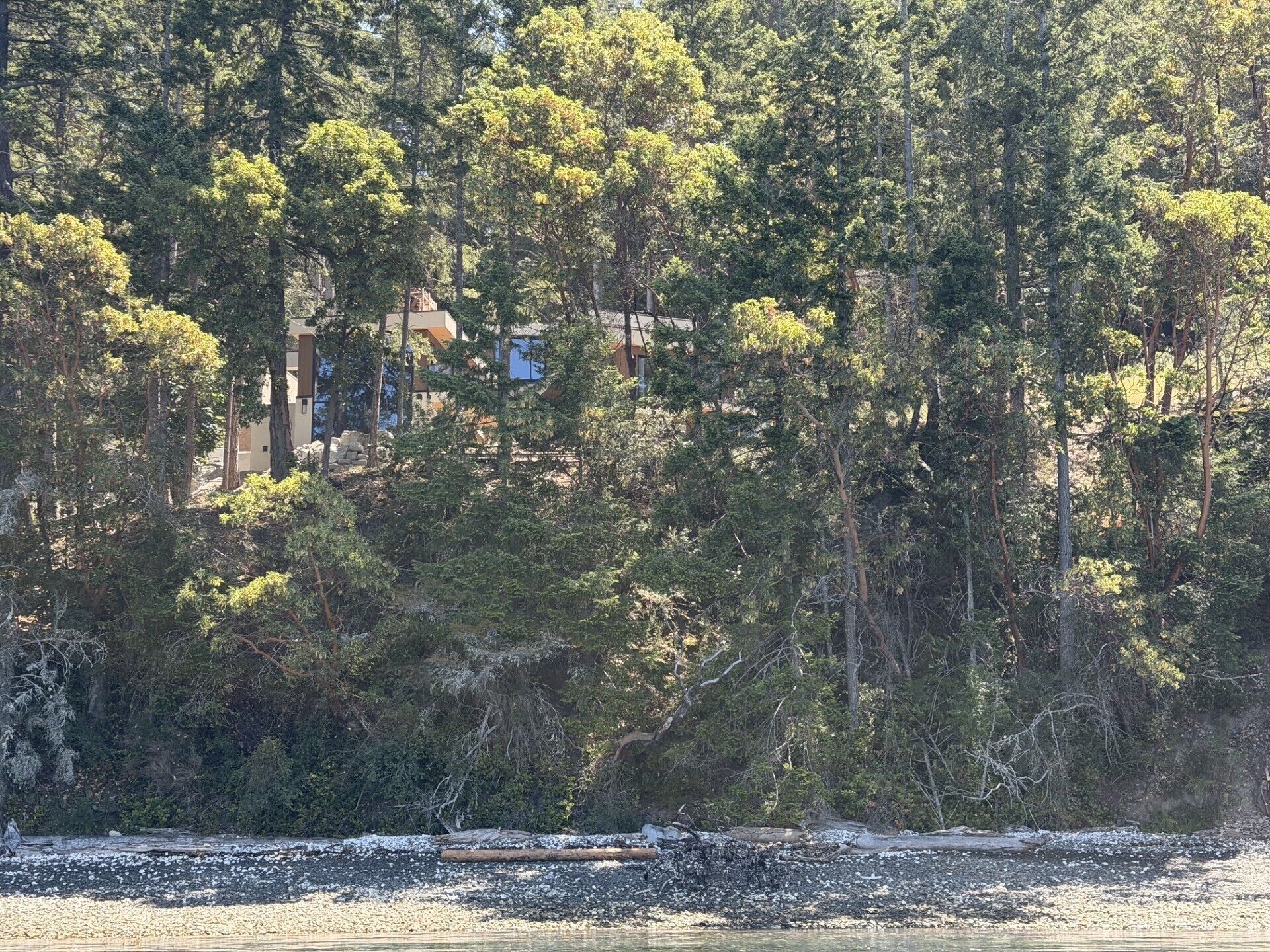 A coastal area with dense trees and a building partially obscured by foliage.