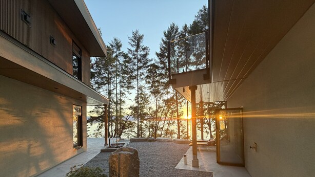 A modern building with a gravel courtyard, large rocks, and a view of trees and water. - Brand new spa resort style waterfront  executive home with luxury amenities (SALT SPRING ISLAND)