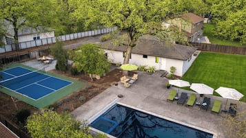 Un patio trasero con cancha de tenis, piscina y mobiliario exterior.