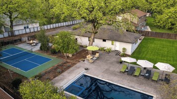 Un patio trasero con cancha de tenis, piscina y mobiliario exterior.