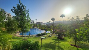 Ein Swimmingpool, umgeben von üppiger Vegetation und Palmen, mit blauem Himmel und Bergen in der Ferne.