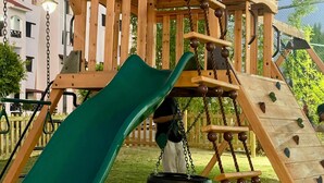 Eine Holzspielanlage mit Rutsche, Schaukeln und Kletterelementen.