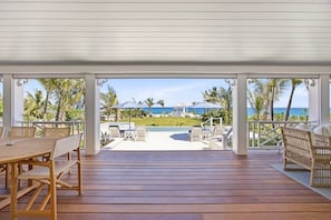 A covered outdoor area with a wooden deck, lounge chairs, and umbrellas, overlooking a beach and ocean. - Pieces of Eight - Hope Town (Hope Town)