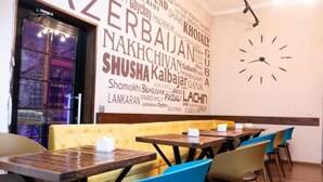 A restaurant interior with tables and chairs, a wall clock, and a large window with a view of the city. - Golden Street Hotel (Baku)