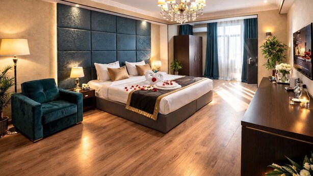 A hotel room with a large bed, a sitting area with a chair, a desk, and a chandelier. - Golden Street Hotel (Baku)