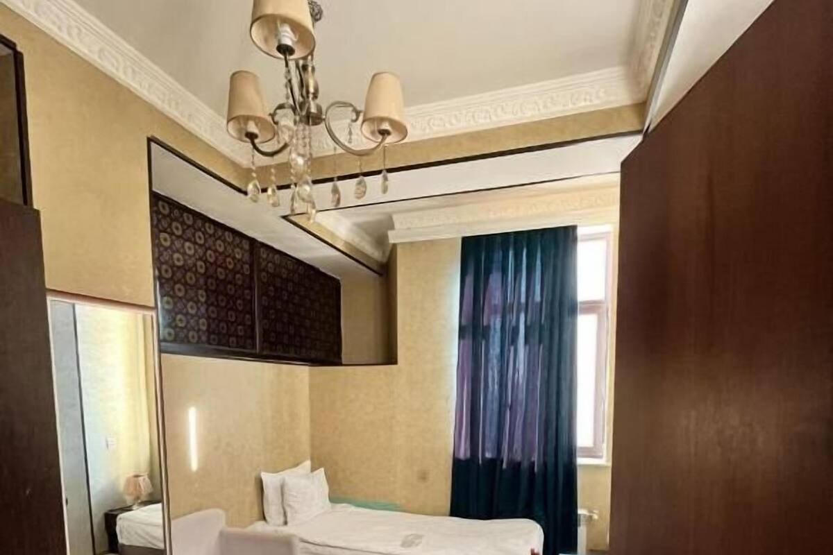 A hotel room with a bed, a chair, a desk, a mirror, and a chandelier.