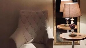 A room with a tufted armchair, a round table with a lamp, and a mirror reflecting a lamp. - Golden Street Hotel (Baku)