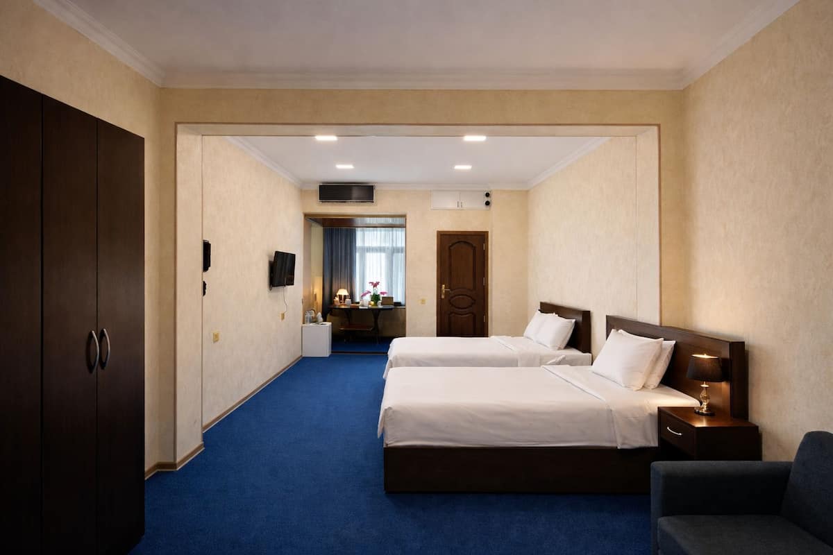 A hotel room with two beds, a desk, a chair, a wardrobe, and a television.