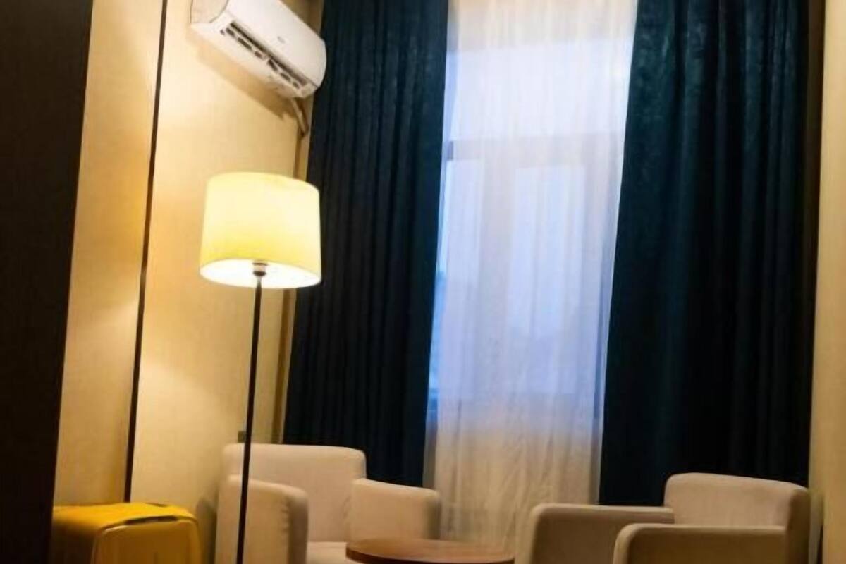 A hotel room with a wooden floor, a small round table, two armchairs, a floor lamp, and a suitcase.