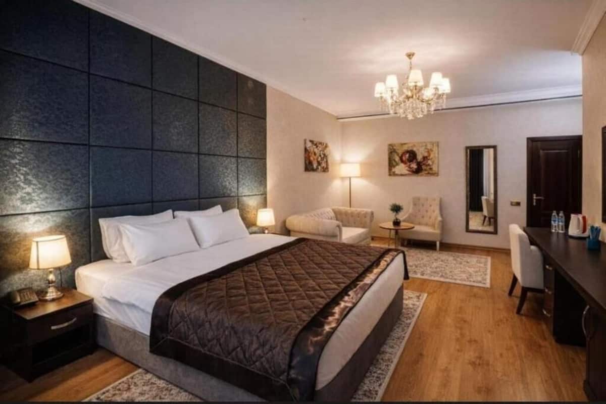 A modern hotel room with a large bed, a desk, a chair, a small table, and a chandelier.