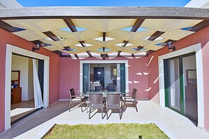 A patio with a table and chairs, a covered area with a geometric ceiling, and a view into the house. - Villa Iris (Corfu)
