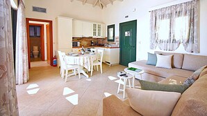 Una sala de estar con sofá, una mesa de comedor con sillas, una zona de cocina y una puerta verde.