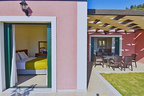 A hotel room with a bed, a nightstand, and a window. There is a patio area with a table and chairs. - Villa Iris (Corfu)