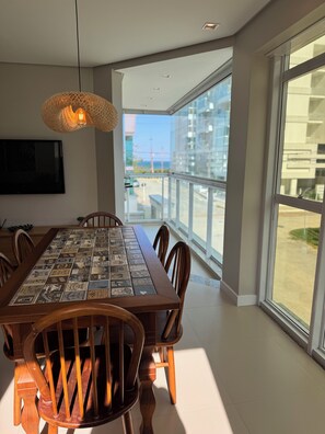 A dining area with a large table covered in a vintage-style tablecloth, surrounded by wooden chairs. - Feet in the Sand, Green Home Palmas (Governador Celso Ramos)