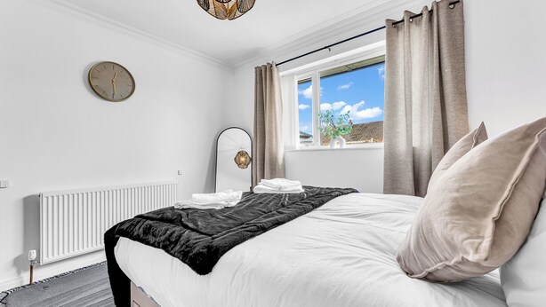 Un dormitorio con una cama, un reloj, un radiador y una ventana con cortinas.