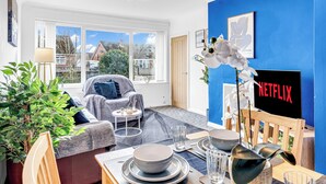 Una sala de estar moderna con una pared azul destacada, un letrero de Netflix, un ventanal grande y una zona de estar acogedora.