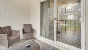 A covered patio with wicker furniture and a glass door leading to a garden.