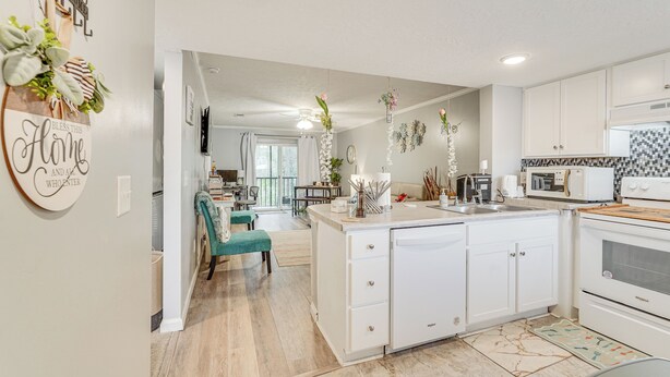 A modern kitchen with white cabinets, a central island, and a dining area with teal chairs.