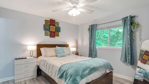 A bedroom with a bed, bedside tables, a ceiling fan, a window with curtains, and a wall with a quilted panel.