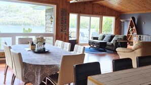 A wooden interior with a dining table, chairs, a sofa, and a TV.