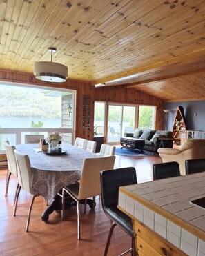 A wooden interior with a dining table, chairs, a sofa, and a TV.