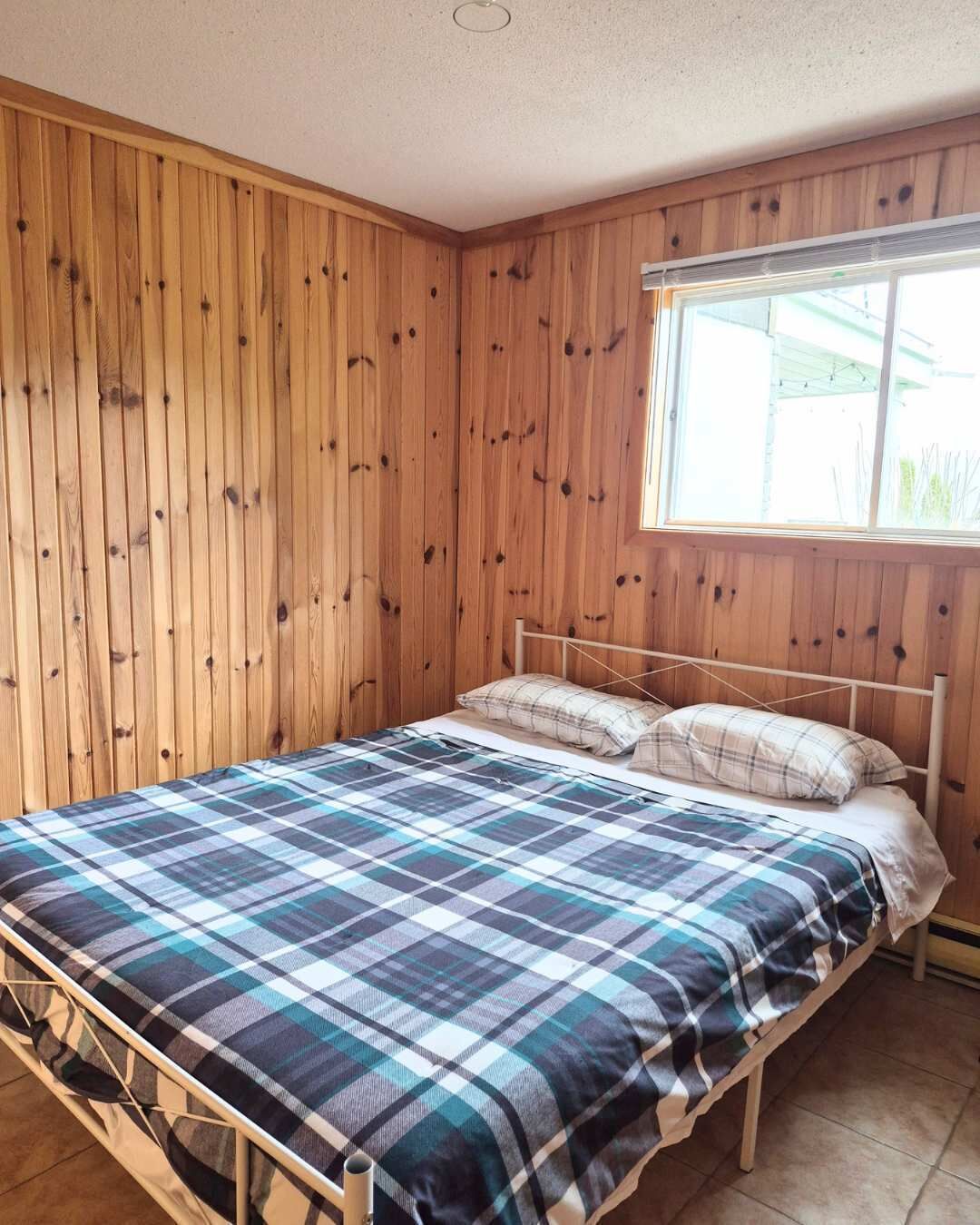 Una cama individual con una colcha escocesa en una habitación con paneles de madera y una ventana.