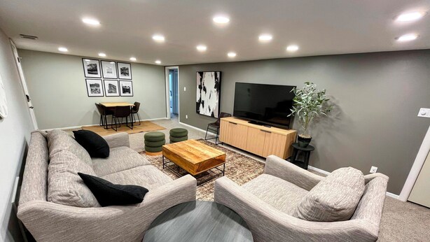A modern living room with a sofa set, a coffee table, a TV, and a dining area. - Cozy 2BR ~15 minutes to Red Rocks (Denver)