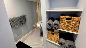 A bathroom with a tiled floor, a towel rack, and shelves with rolled towels and woven baskets. - Cozy 2BR ~15 minutes to Red Rocks (Denver)
