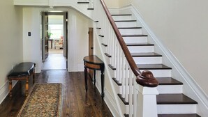 A staircase with white railings and dark wooden steps, leading to a room with a door and a bench. - Bourbon Country Escape! Spacious Home w/ Fire Pit (Taylorsville)