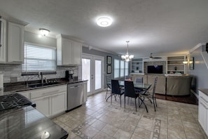 A modern kitchen with white cabinets, a dining area with a glass table, and a TV in the living room. - 3 Mi to Butler U: Family-Friendly Indy Home (Indianapolis)