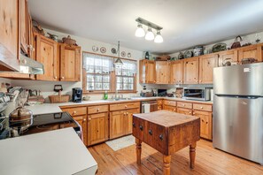 Eine Küche mit Holzausstattung, einem Edelstahlkühlschrank, einem Holztisch und einem Fenster mit Spitzenvorhängen.