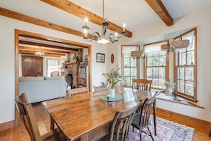 A wooden dining table with chairs, a chandelier, and a view of the outdoors through large windows. - Vintage Home Nestled in the Woods of Smoky Mtns (Marble)