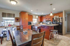 A modern kitchen with wooden cabinets, a central island, bar stools, and a refrigerator. - Fishing Dock! 'Oarhouse South' Near Venice Marinas (Buras)